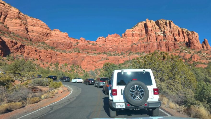 Traffic on a Sedona road near red rock cliffs and trailhead parking