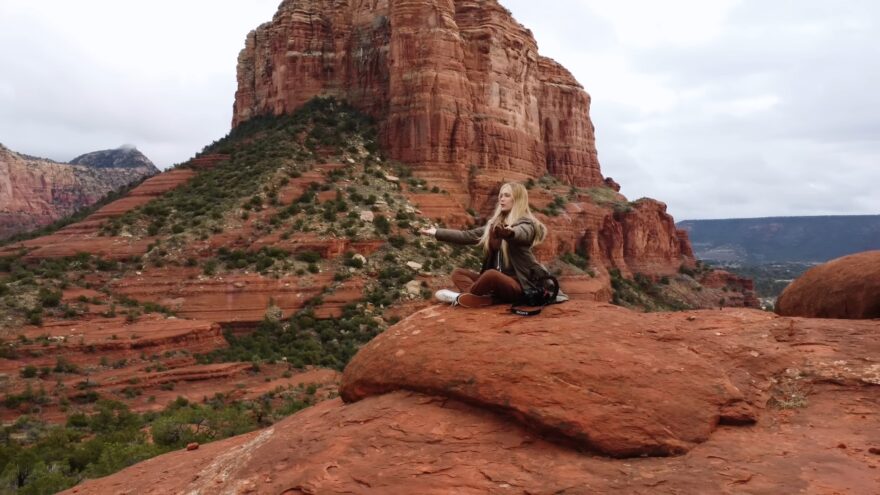 Woman meditating on red rocks at one of Sedona's vortex sites with sandstone cliffs in the background