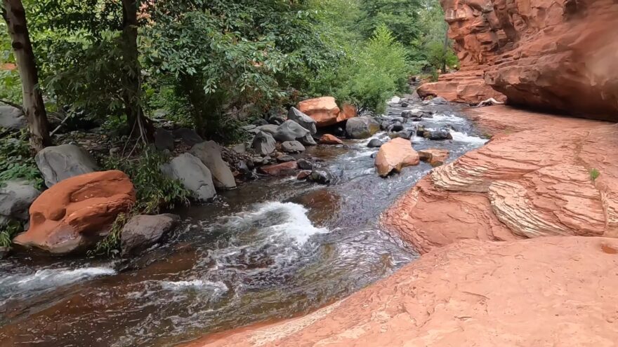Water flows through Slide Rock State Park between red sandstone walls and trees